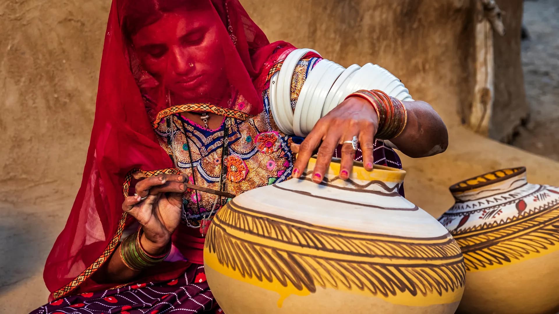 Rajasthani woman in a red odhni hand-painting clay pots