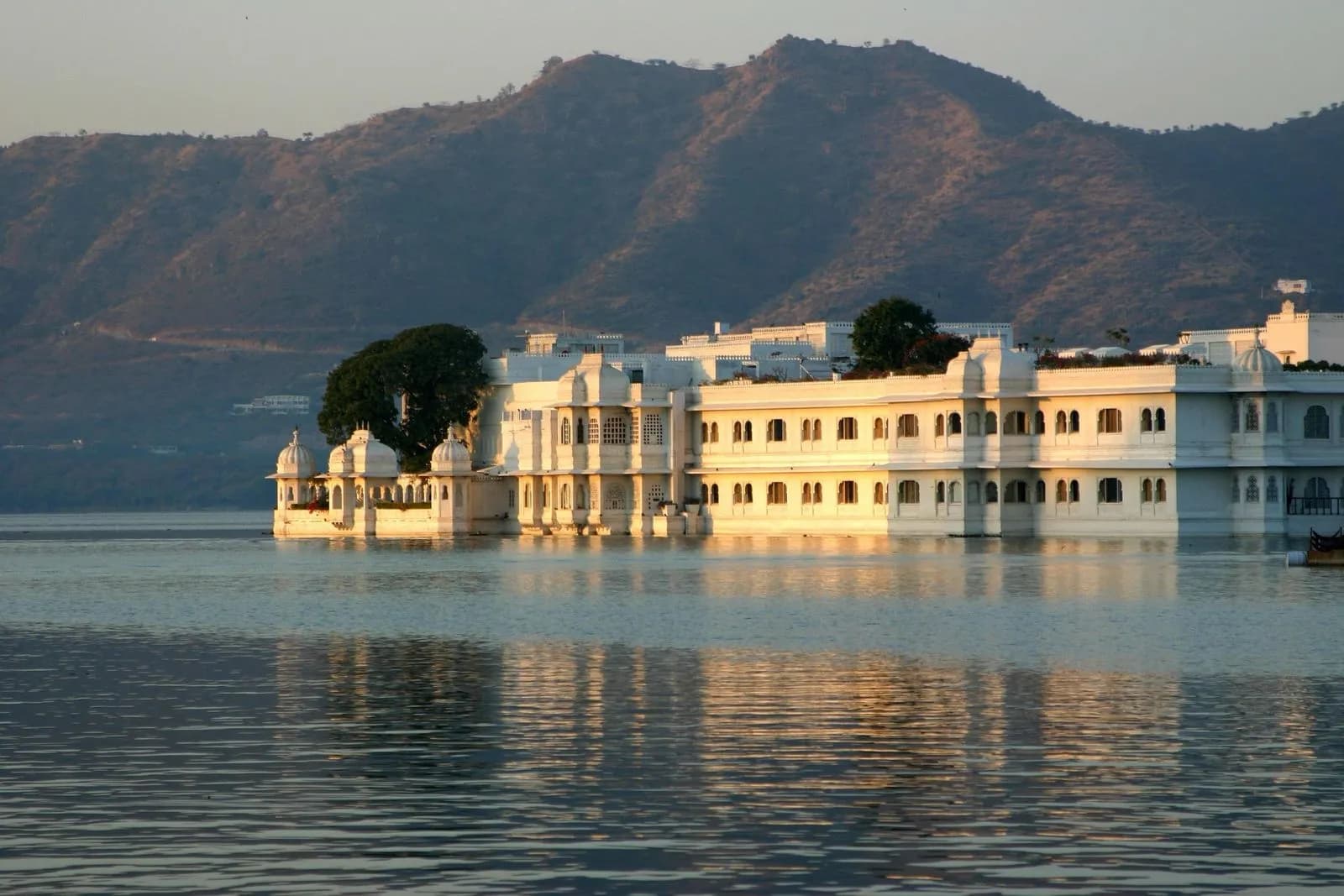 Lake Palace glowing at golden hour on Lake Pichola with the Aravalli hills behind
