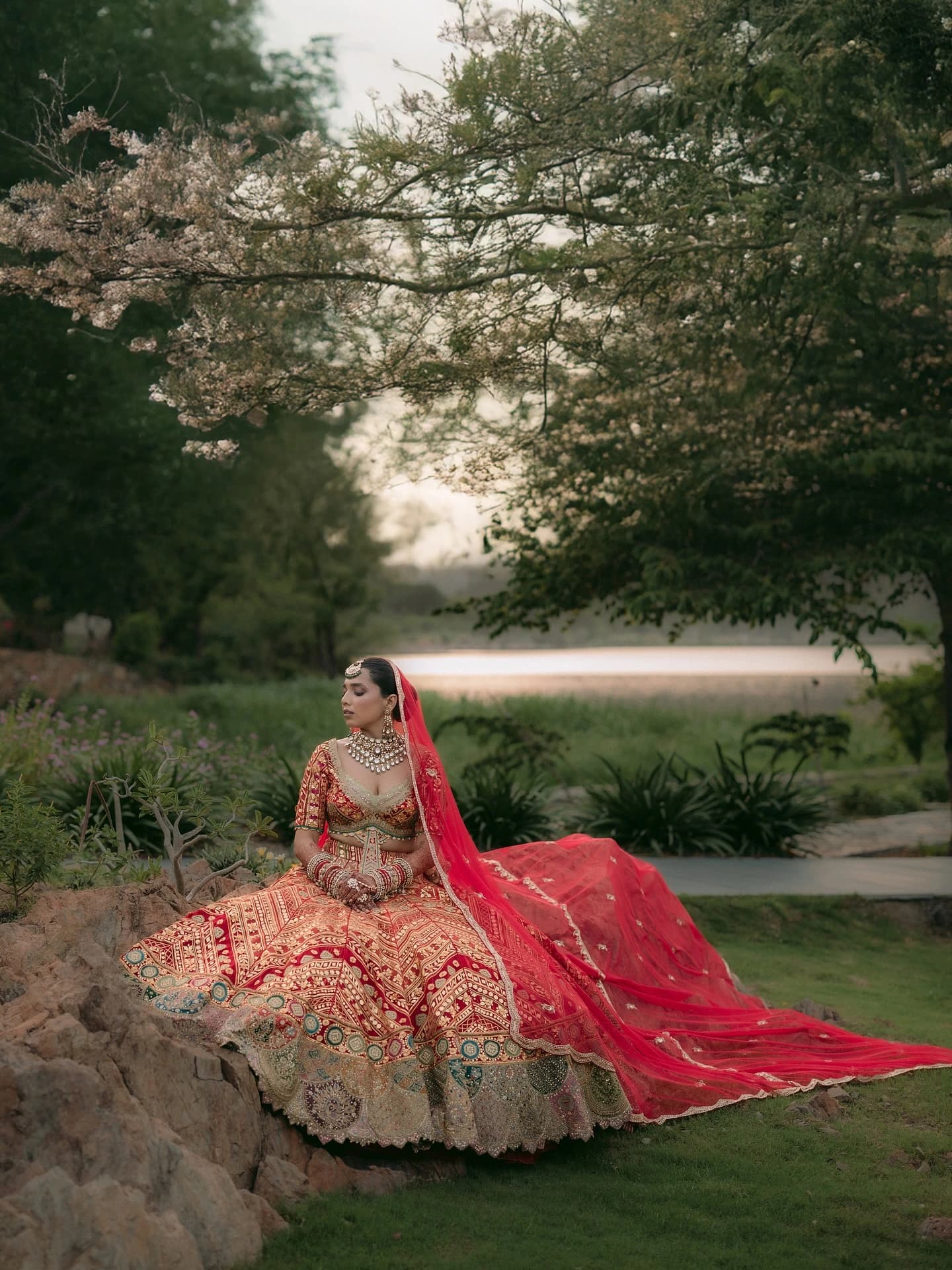 Bride in a red lehenga sitting in a garden in Udaipur