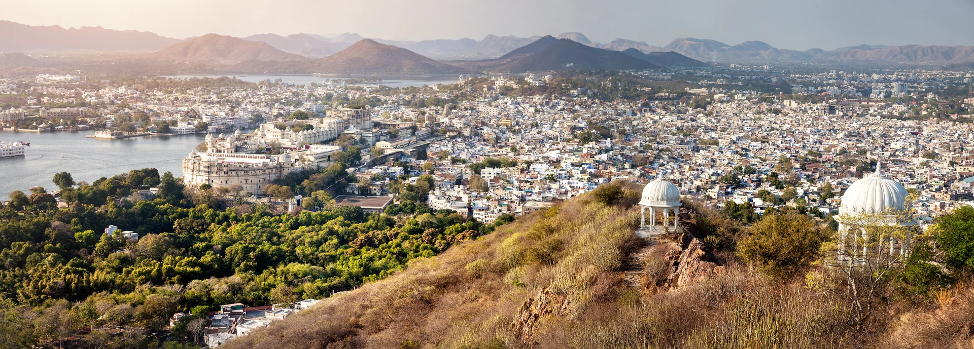 Panoramic view of Udaipur city from a hilltop, white domes in the foreground and lakes and hills beyond